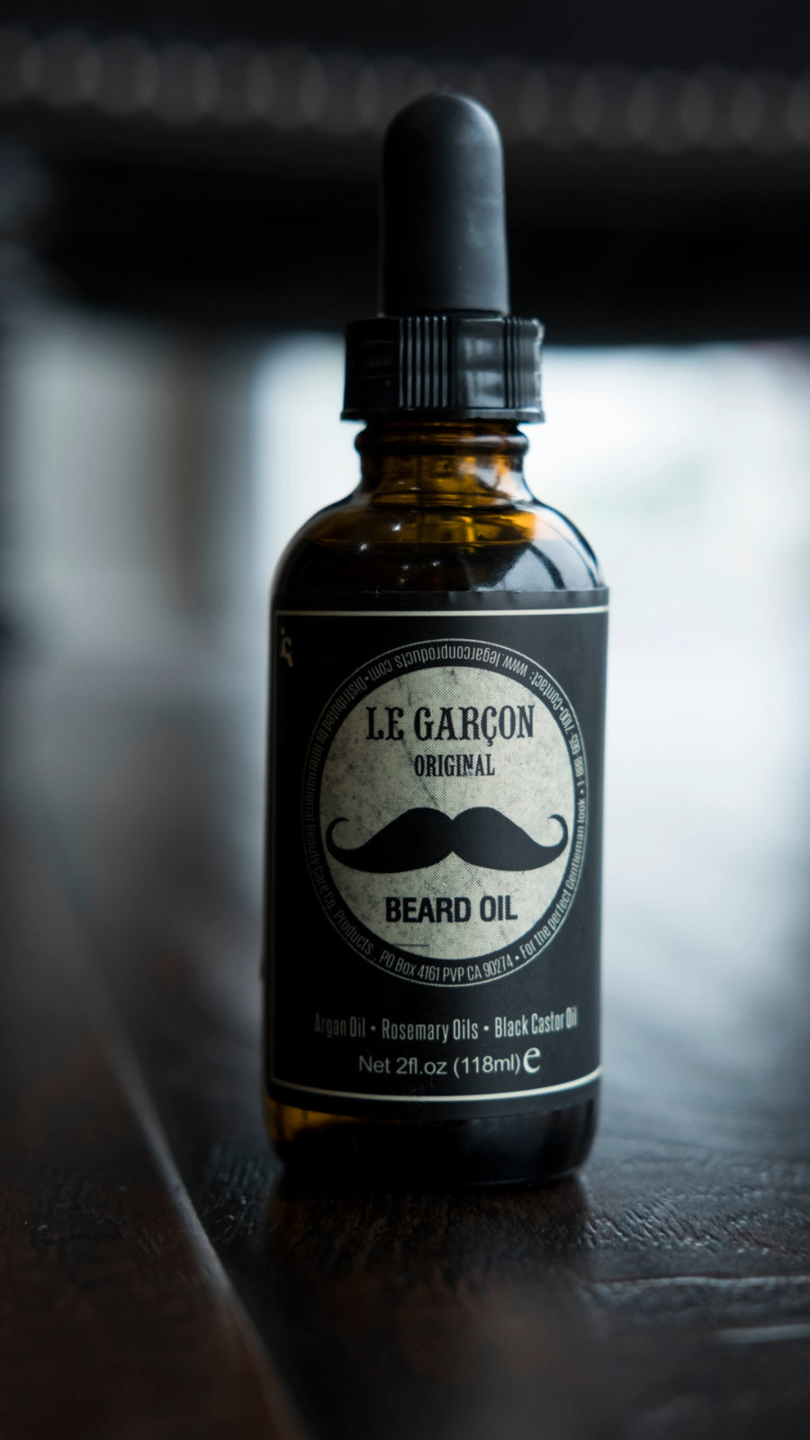 Beard oil bottle labeled 'Le Garçon Beard Oil' resting on a rustic wooden surface